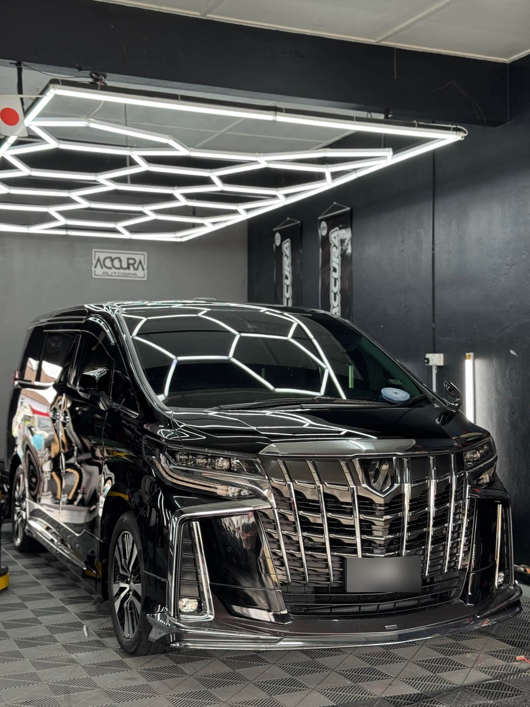 Toyota Alphard hitam berkilat di bawah lampu heksagon Accura