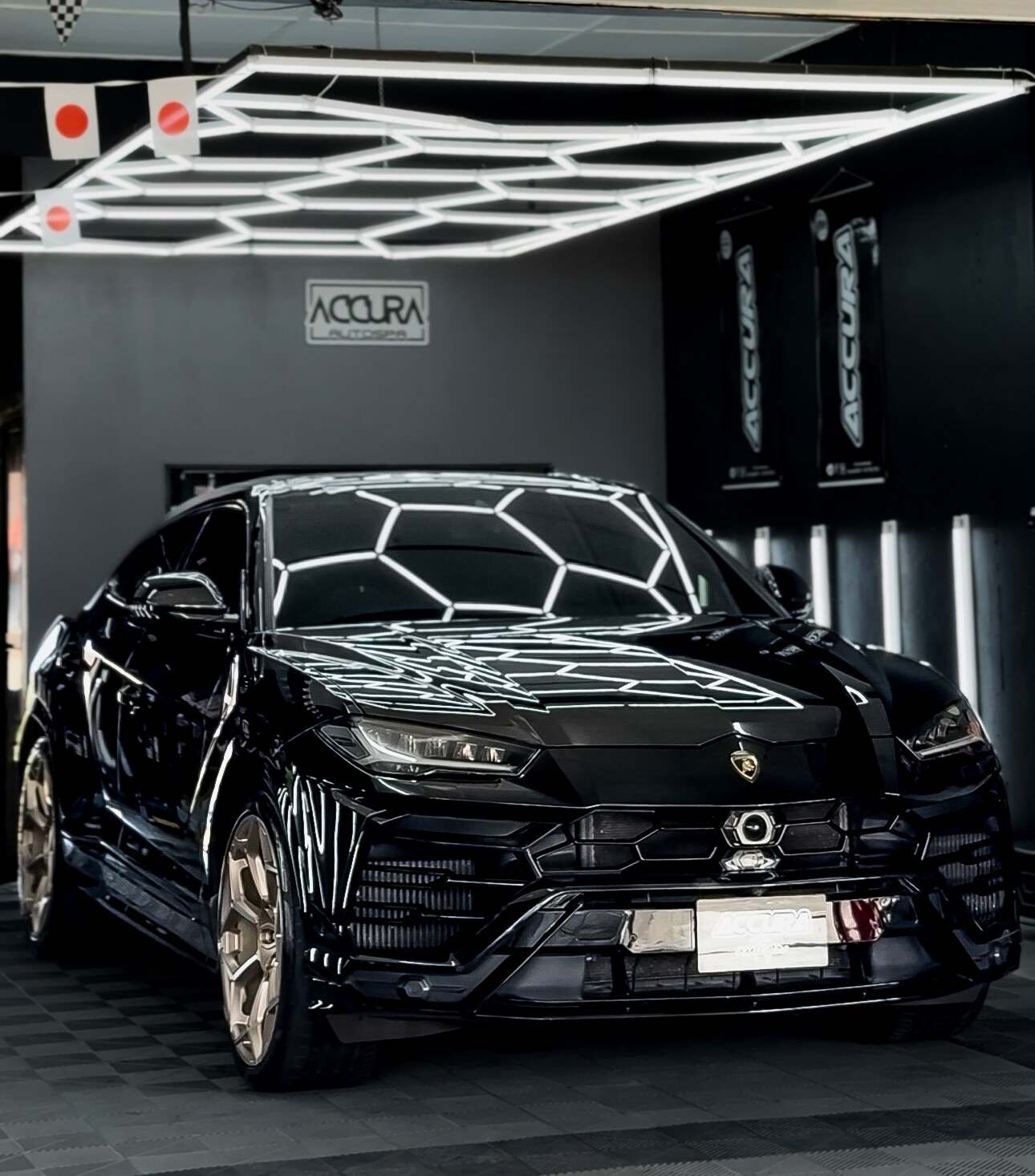 Lamborghini Urus hitam dengan rim emas di bawah lampu heksagon